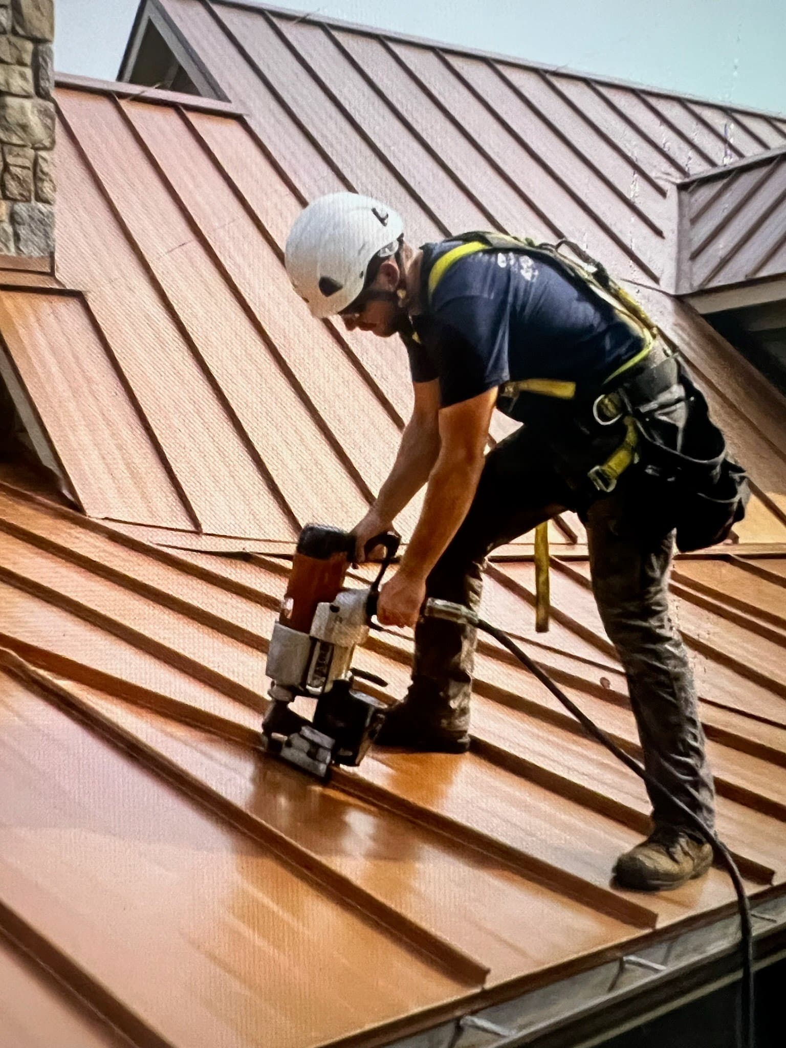 A roofer screwing down a metal roof panel